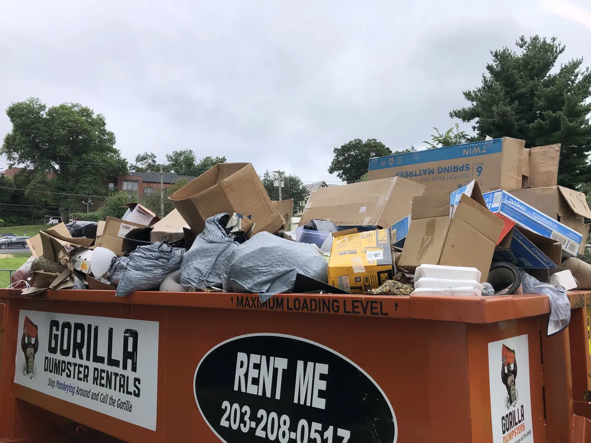 Unsafe dumpster loading example with debris piled high above the container walls
